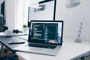A-MacBook-with-lines-of-code-on-its-screen-on-a-busy-desk-scaled